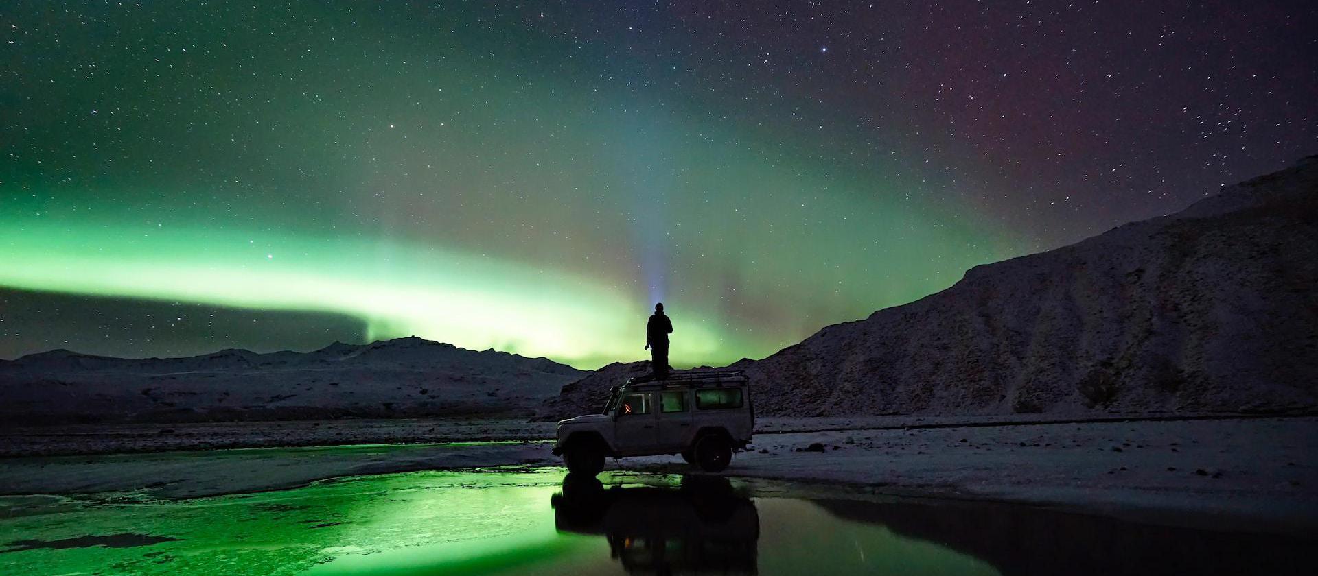 man standing on SUV watching northern lights