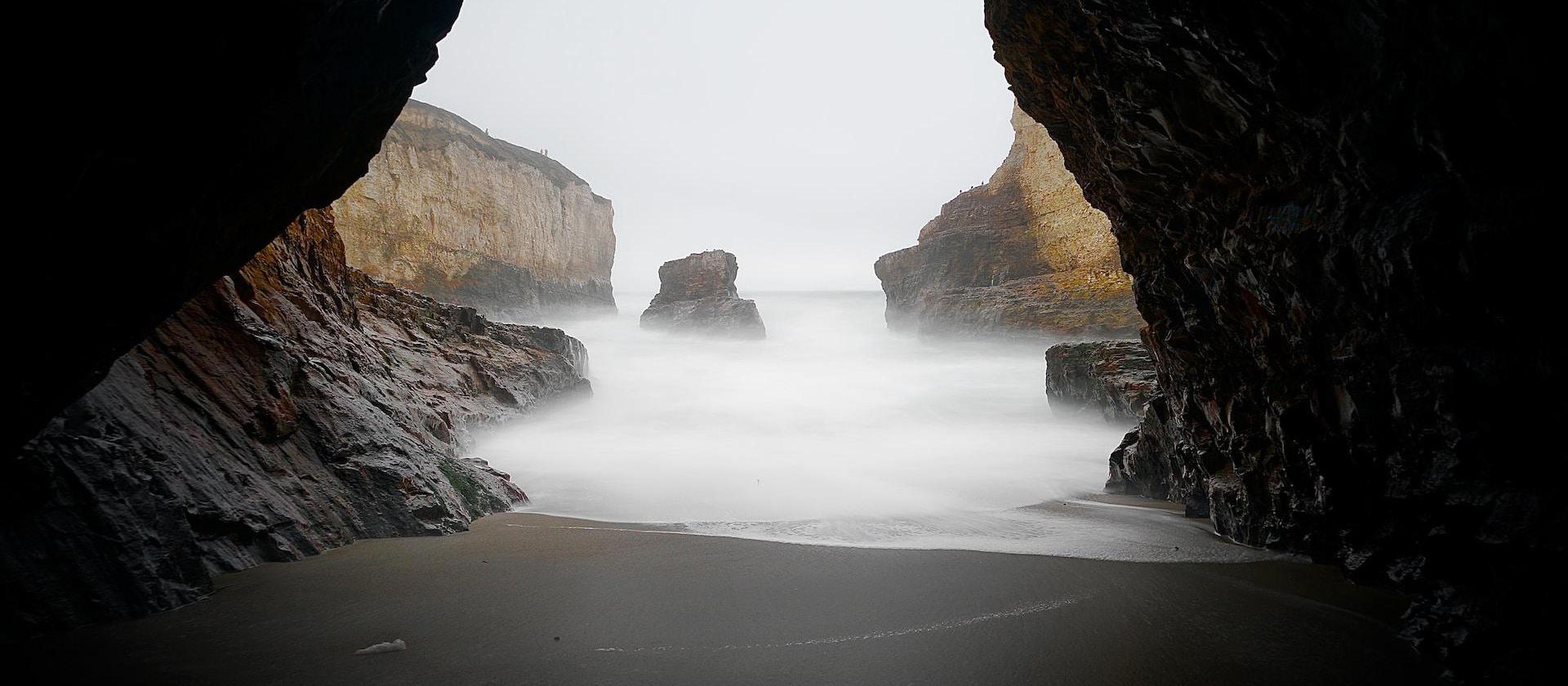 brown cave near body of water during daytime.