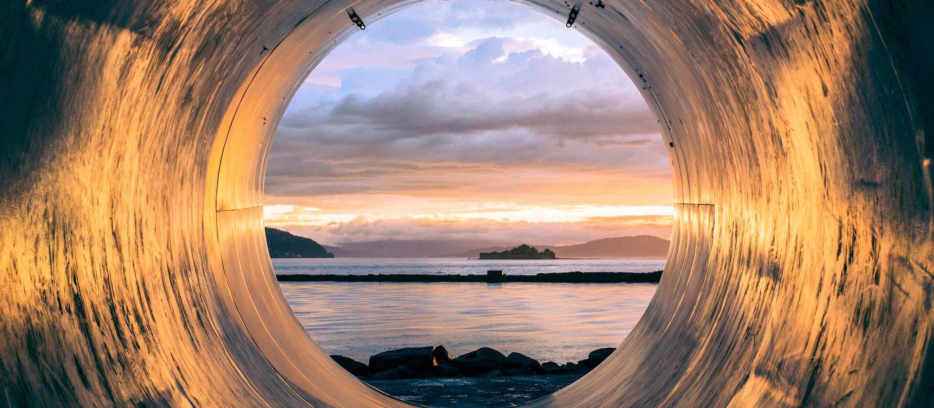 Image of body of water and sunset can be seen through the tunnel.