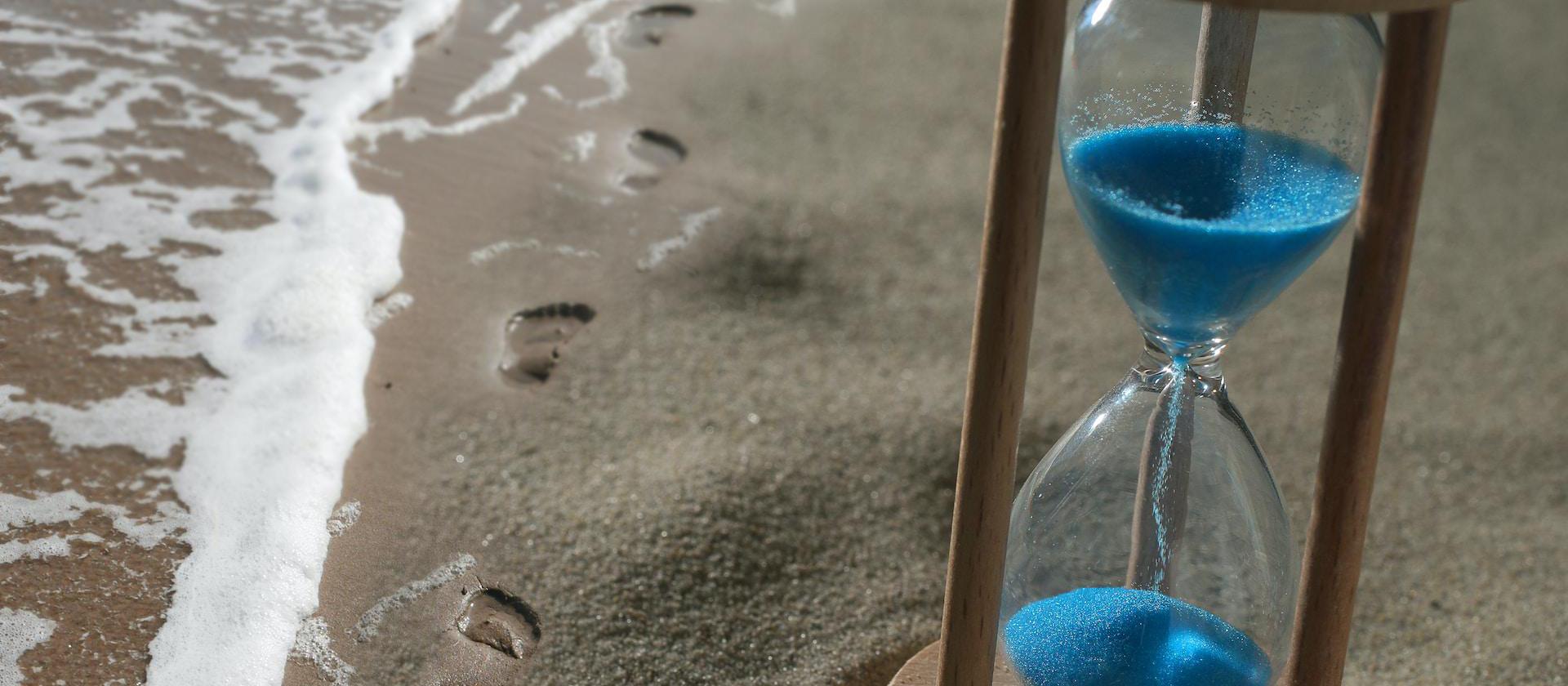 brown hourglass with blue sand on shore next to sea.