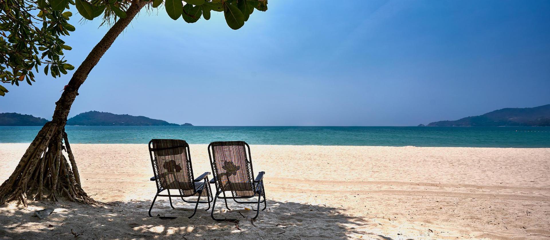 a couple of chairs sitting on top of a sandy beach